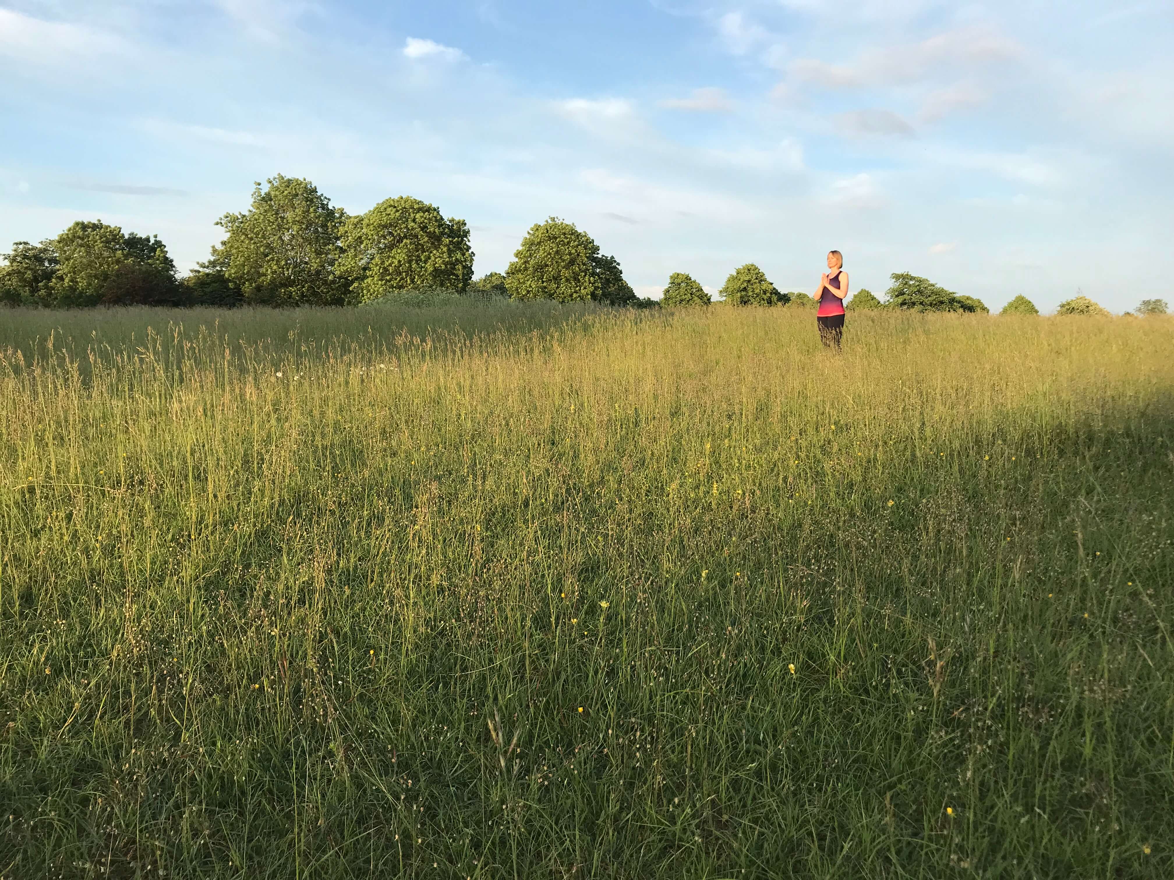 Woman practising Sun Salutations in a field of grass